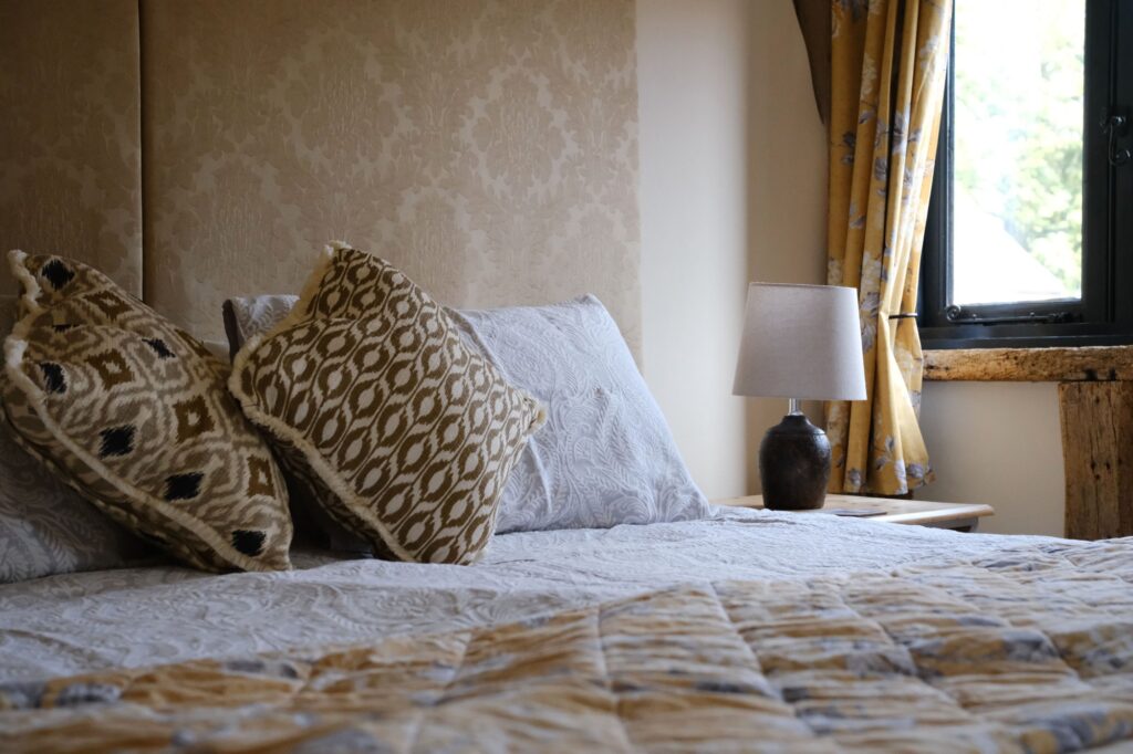 A double bed with patterned cushions and a bedside lamp by the window