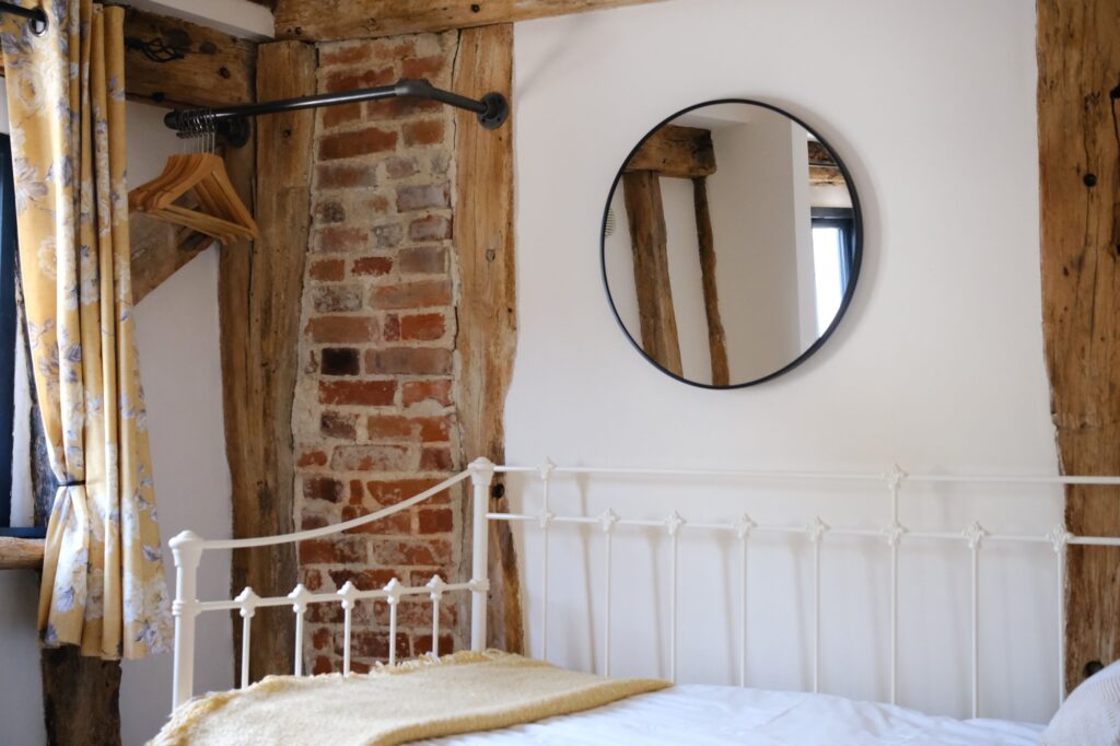 A white iron day bed beside exposed brick and oak beams, with a round mirror