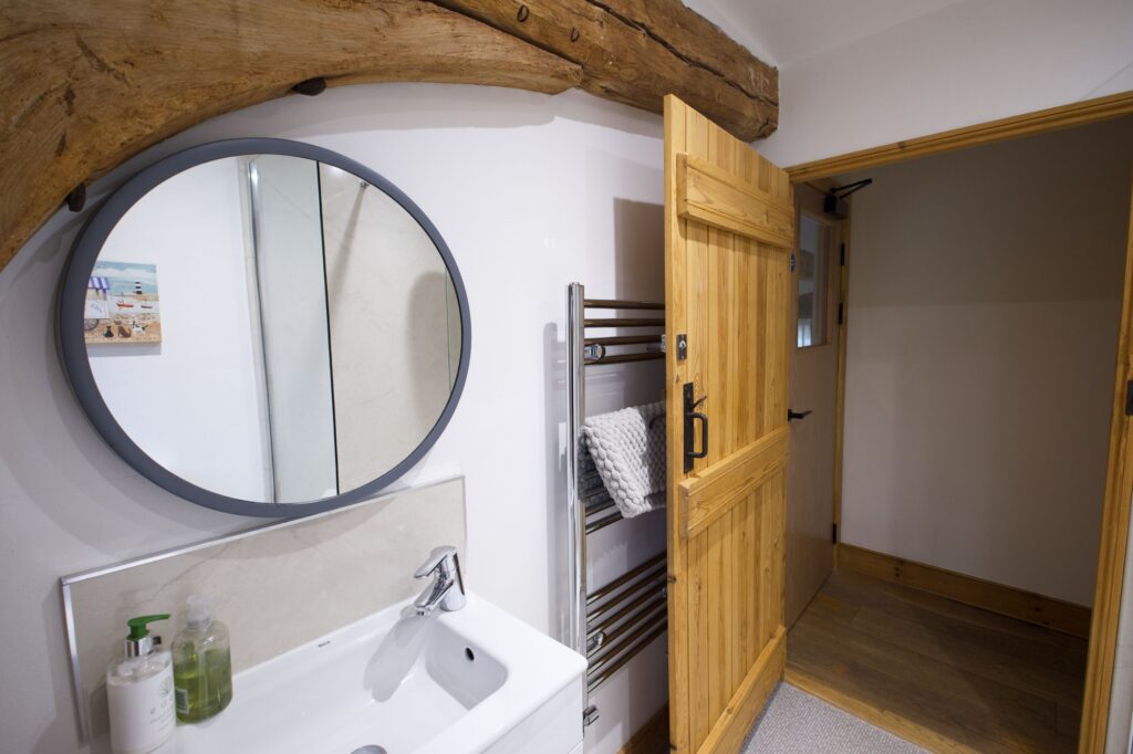 The en-suite shower room with a round mirror under a curved oak beam