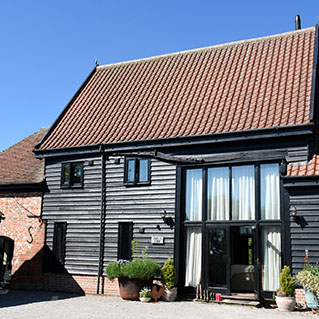 The front of Owls End, with its tall glazed doors and potted plants on the gravel