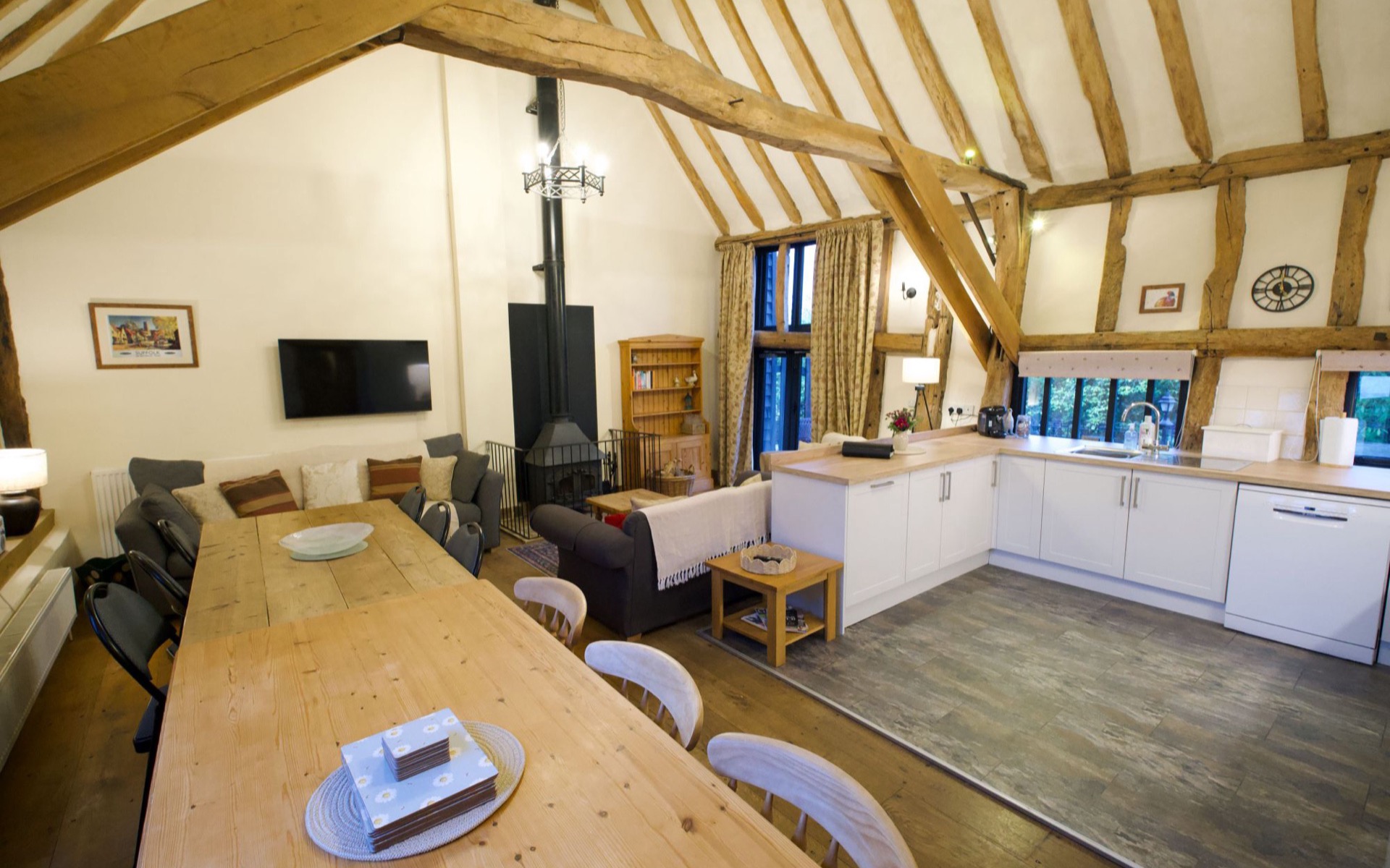 The open-plan living space at Tithe Barn, with the dining table, wood burner and kitchen under the beams