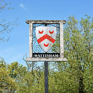 The Wattisham village sign, with red crescents on a white shield