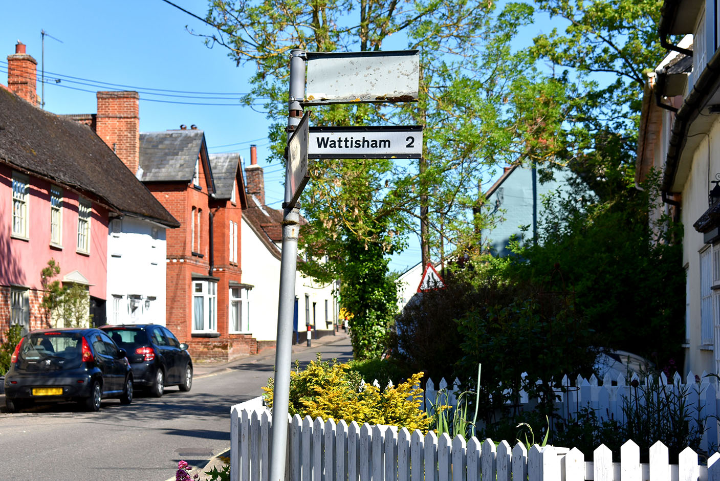 A village signpost reading Wattisham 2, on a street of Suffolk cottages