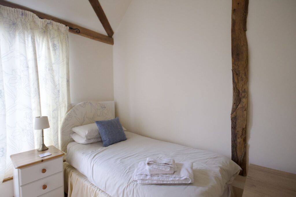 A single bed in the twin room, with a bedside lamp and an oak post