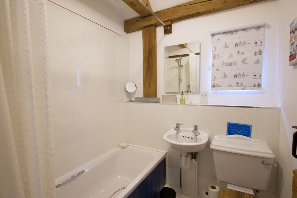 The bathroom with a bath and shower over it, beneath an oak beam