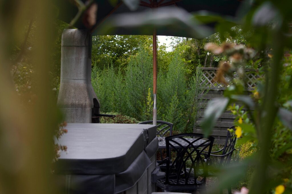 The Willow hot tub and patio table seen through the garden planting