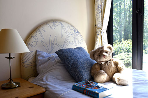 A teddy bear and a book on a bed by the window