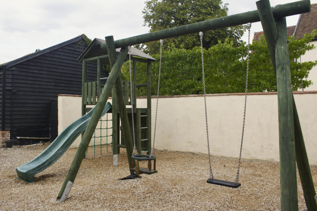 The swings and climbing frame in the walled playground beside the barns